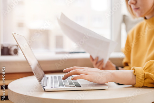 Woman working with papers and on a laptop, typing on keyboard, close up