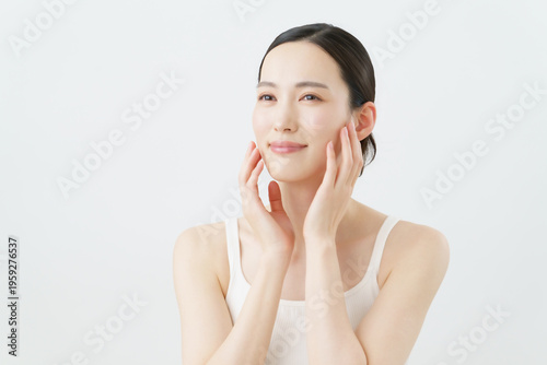 Fotografija 白背景の頬に手を当てる若い女性のスキンケアイメージ