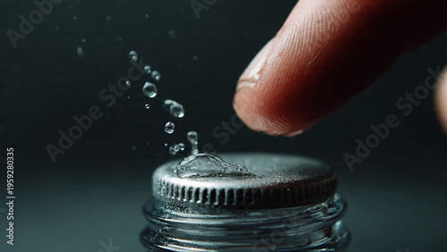 Finger touches bottle cap causing water droplets to splash upwards