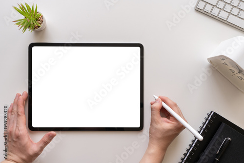 Top view of a person using a digital tablet with blank white screen on a modern white desk. Featuring a stylus, notebook, and keyboard, perfect for mockups, remote work, and creative business projects