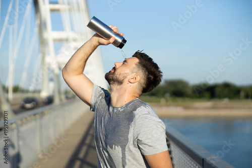 Sweaty male runner pouring water on his face to cool down and rehydrate after an exhausting urban bridge workout in summer heat