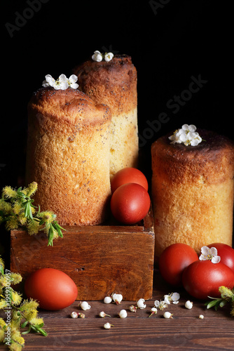 Homemade easter cakes with spring flowers, fresh willow bouquet and red eggs on dark moody rustic background, traditional russian holiday food, cottagecore aesthetics, slow living celebration concept