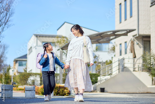 住宅街を手を繋いで歩く母親とランドセルを背負った女の子