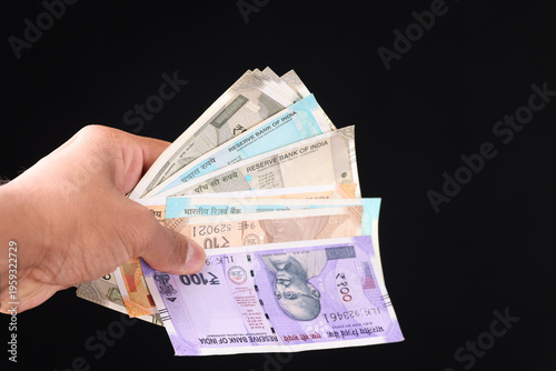 Fotografía Hand holding a variety of Indian currency notes including 100, 200, and 500 denominations, Concept of diverse financial savings and cash payment on black background