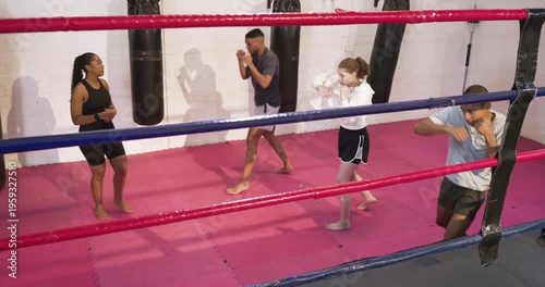 After entering red ring, diverse boxing coach and trainees practicing jab footwork drills toward bag