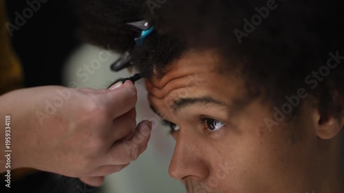 Professional hairdresser working on a client's afro hair. Close-up on the patient face of a mixed-race man getting dreadlocks extensions