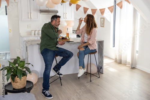 Couple sitting on bar stools at marble kitchen island celebrating with wine and charcuterie board