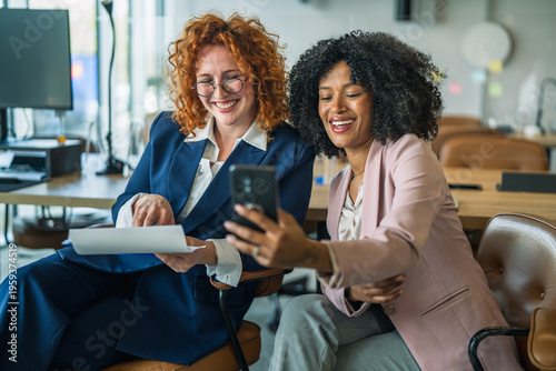 Diverse business women collaborating, smiling, and using a smart phone
