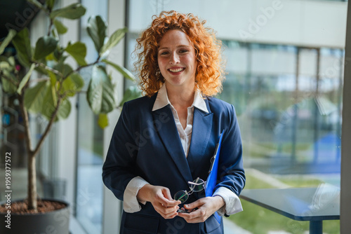 Confident businesswoman holding clipboard and eyeglasses in office