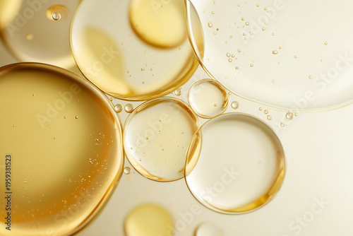 Close-up of transparent yellow oil droplets on a light background. The droplets vary in size and contain small bubbles, creating a textured appearance