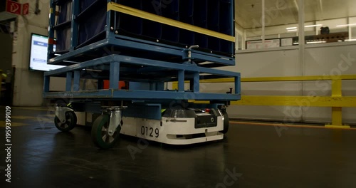 Autonomous mobile robot transporting a heavy blue cargo rack through a large industrial warehouse facility
