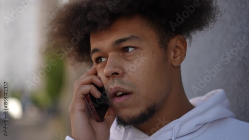 Serious young mixed race man with an afro hairstyle having a phone conversation. His expression shifts from smiling to concerned outdoors