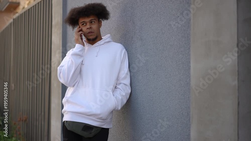 Young african american man with afro hair leaning against a wall talking on the phone. Trendy guy in urban scenery having conversations