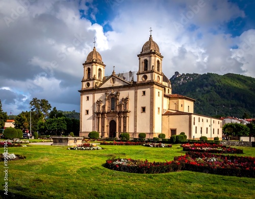 A grand European church with ornate details, twin bell towers, a facade of architectural elegance, and a landscape with vibrant flowers