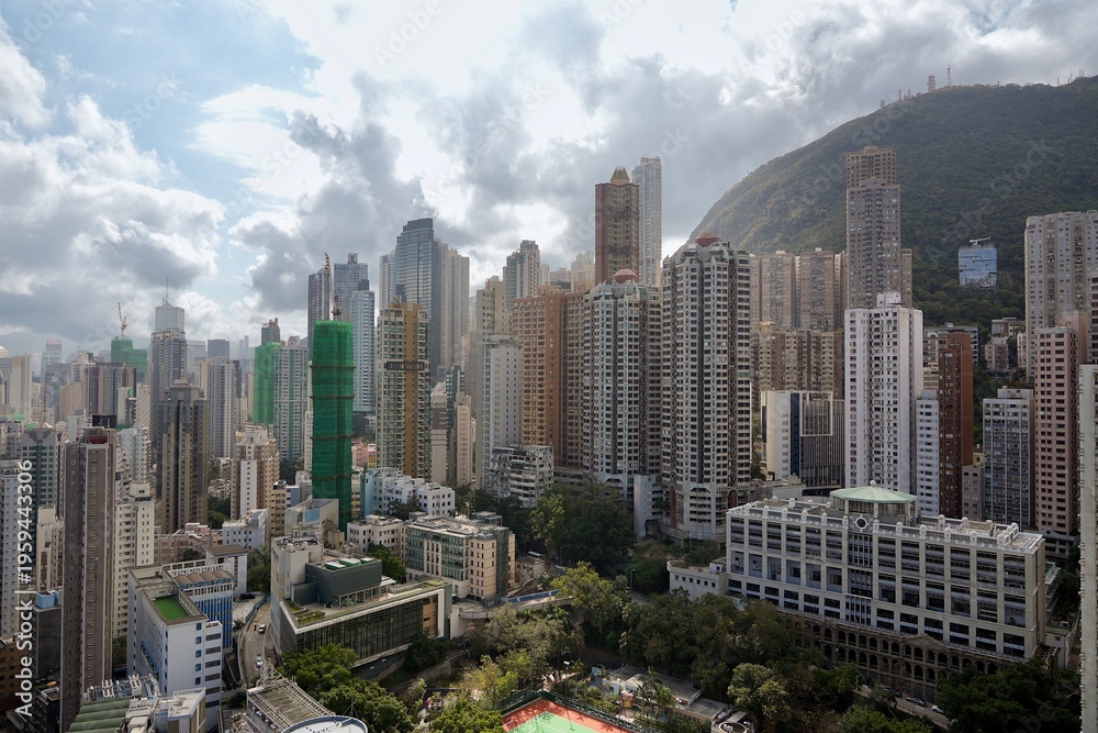 Obraz premium A sprawling view of high-rise apartment buildings and office towers nestled against the steep green hills of Hong Kong Island