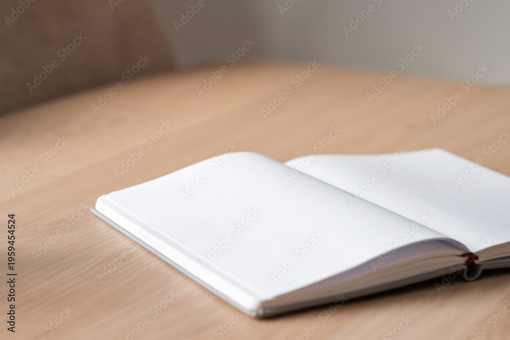 Fototapeta premium Open notebook with empty white sheets mockup on plain wooden table background with natural sunlight and soft focus. Neutral backdrop with warm natural tones