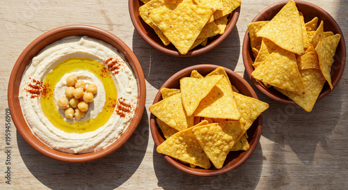 top view of delicious hummus with chickpeas and nachos in bowls on beige wooden table, panoramic
