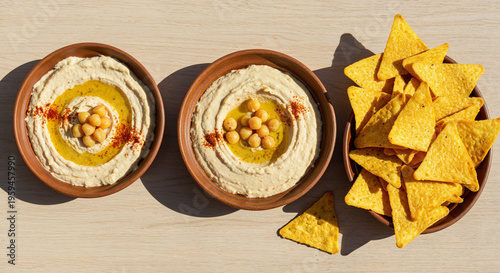 top view of delicious hummus with chickpeas and nachos in bowls on beige wooden table, panoramic