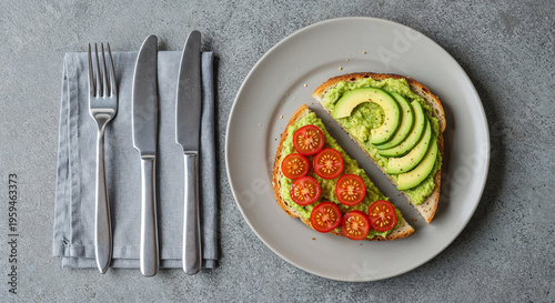 top view of toast with avocado and cherry tomato, fork and knive isolated on grey