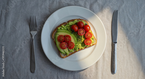 top view of toast with avocado and cherry tomato, fork and knive isolated on grey