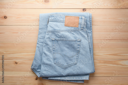 Folded light blue jeans with blank leather label on wooden surface create clean apparel mockup for denim branding and retail.