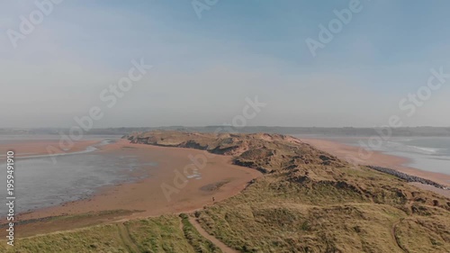 Aerial drone gliding over vast sandy dunes and calm water at Tramore, Ireland, revealing expansive coastal landscape and serene natural beauty, perfect for travel and nature exploration.