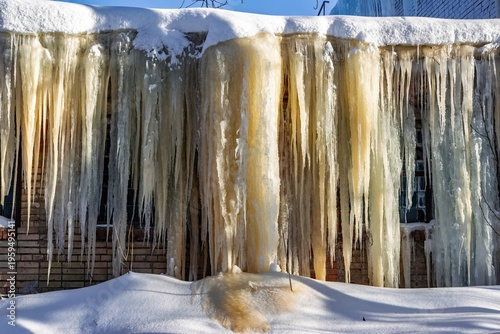 Tableau sur toile Massive frozen icicles cascade down a building facade, glistening in the cold morning light