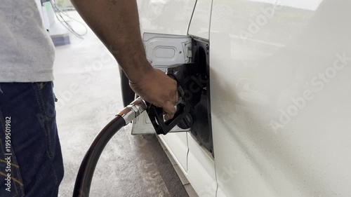 A close-up shot of a man refueling a van himself. The text on the fuel cap in Thai translates to 
