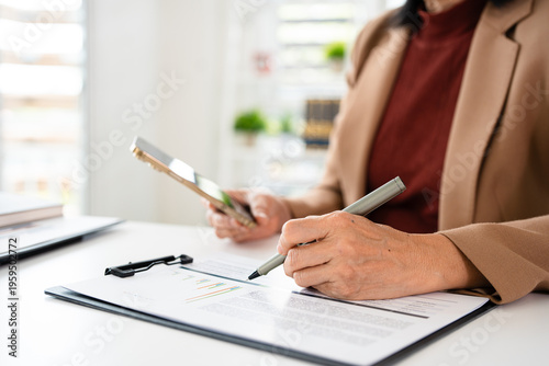 Close up of a woman hand holding smartphone and holding pen writing in notebook . Working in office.