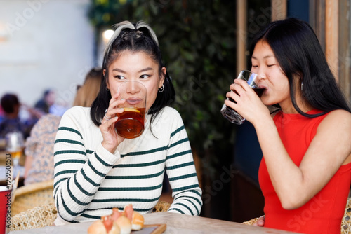 Asian women chatting. Casual portrait of two women sipping drinks and having friendly chat outdoors