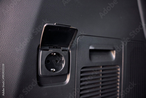 Quadro su tela Close-up of a built-in 230V AC power outlet with a protective plastic cover, located in the black leather-trimmed interior of a modern SUV trunk or cabin