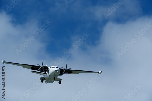 Twin-engine short-range transport aircraft on final approach to landing in blue sky with clouds. Regional twin-prop airplane landing in bright blue sky with fluffy clouds