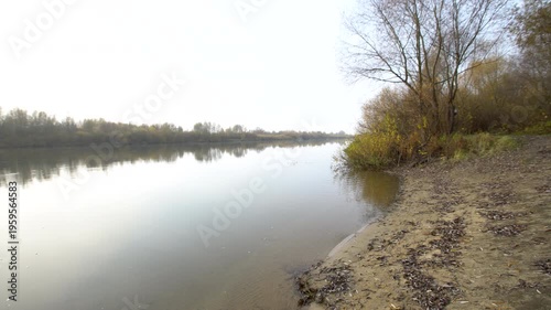 In autumn, the river stretches through a quiet landscape. Trees line the shore and the water reflects the surroundings.