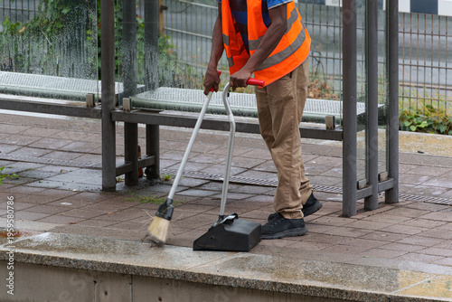 Canvastavla Street cleaner in safety vest sweeping sidewalk near public transport stop