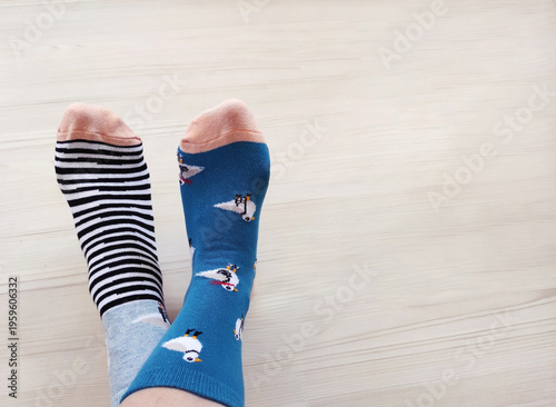 Person’s legs in colorful cotton socks on a light wooden background. Cozy home scene with crossed legs and a minimalist backdrop.