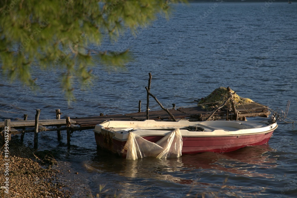 Obraz premium Boat by wooden pier with pine branch framing the coastal scene