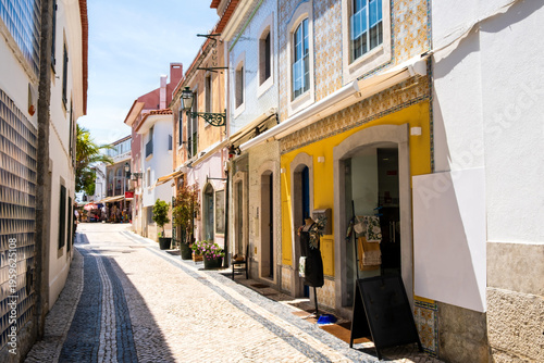 Traditional Portuguese narrow street with azulejos tiles facades and yellow storefronts in Cascais old town, Portugal. Sunlit cobblestone path with retail shops