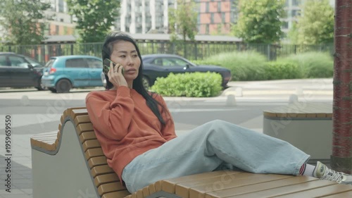 Calm Woman Talking On Smartphone While Relaxing On Bench In Modern City