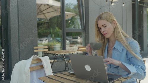 Focused Woman Typing On Laptop And Drinking Coffee At Outdoor Street Cafe