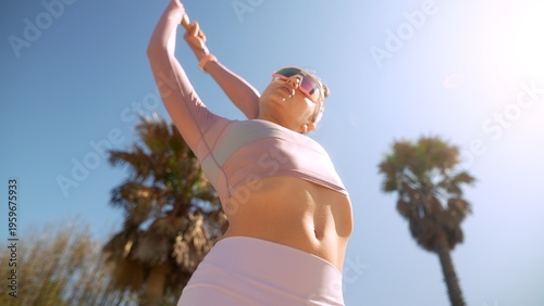 Woman in pink top and white shorts exercising beneath palm trees