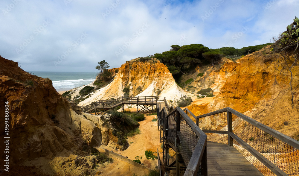 Obraz premium Scenic view of cliffs in Portugal with ocean waves and a wooden pathway leading through the rugged landscape.