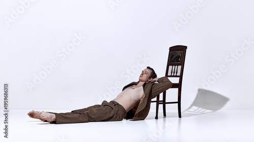 Φωτογραφία Male dancer lying on floor near chair in relaxed pose in minimal studio