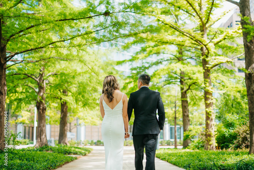 Tableau sur toile Wedding couple walking under bright green trees in park on the wedding day