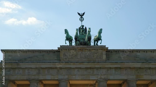 BERLIN, GERMANY - MARCH 23 2026: Panning shot close up of the Quadriga statue on top of the Brandenburg Gate with dramatic sunlight and lens flare in the background
