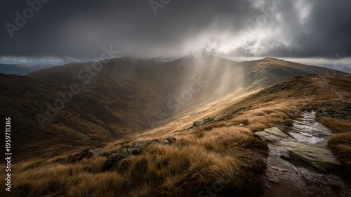 Dramatic sunbeams pierce stormy clouds over rugged mountain landscape with golden grass