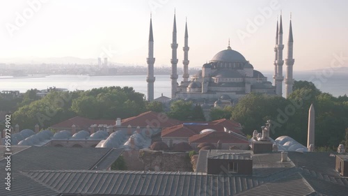 The Blue Mosque stands prominently with multiple minarets overlooking the Bosphorus and Istanbul skyline. Clear morning light highlights domes, rooftops, and surrounding greenery in a calm urban scene
