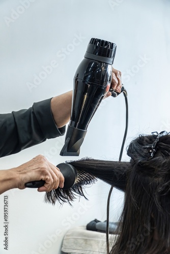 Woman Having her Hair Straighten with a Brush and a Hair Dryer. Hairdresser drying clients hair working with professional tools. Hairdresser dries long hair in a beauty salon