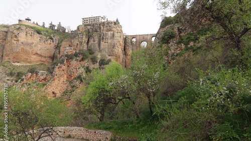 Scenic view of the historic Puente Nuevo bridge and white buildings perched on cliffs, seen from the lush green walking paths of Ronda, Malaga.