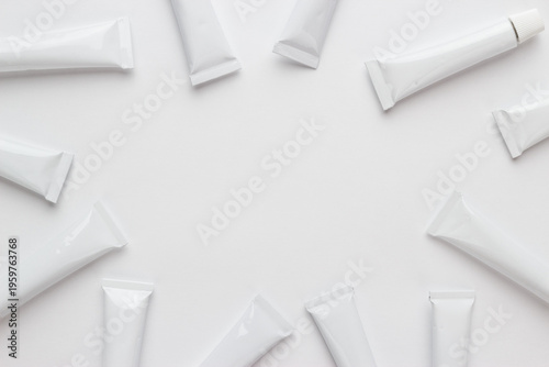 Flat lay photo of oil paint tubes on light grey background with copy space in the center. White oil paint tubes with labels removed arranged around blank center on clean white background.
