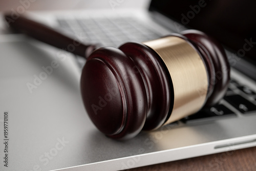 Closeup photo of wooden gavel on modern laptop keyboard, symbolizing themes of legal charges or lawsuit in computer tech industry.